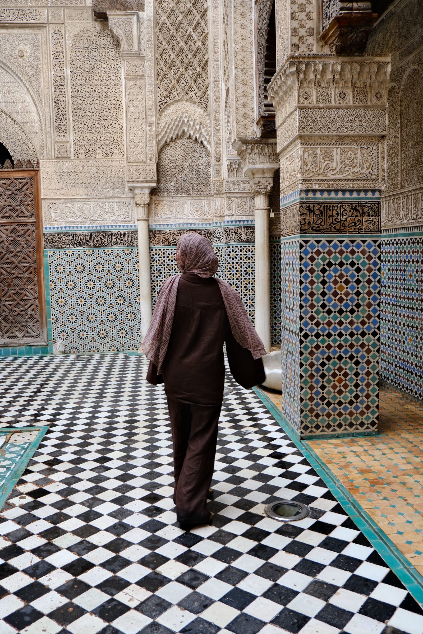 A traveller walking through a tiled madrasa courtyard in Morocco